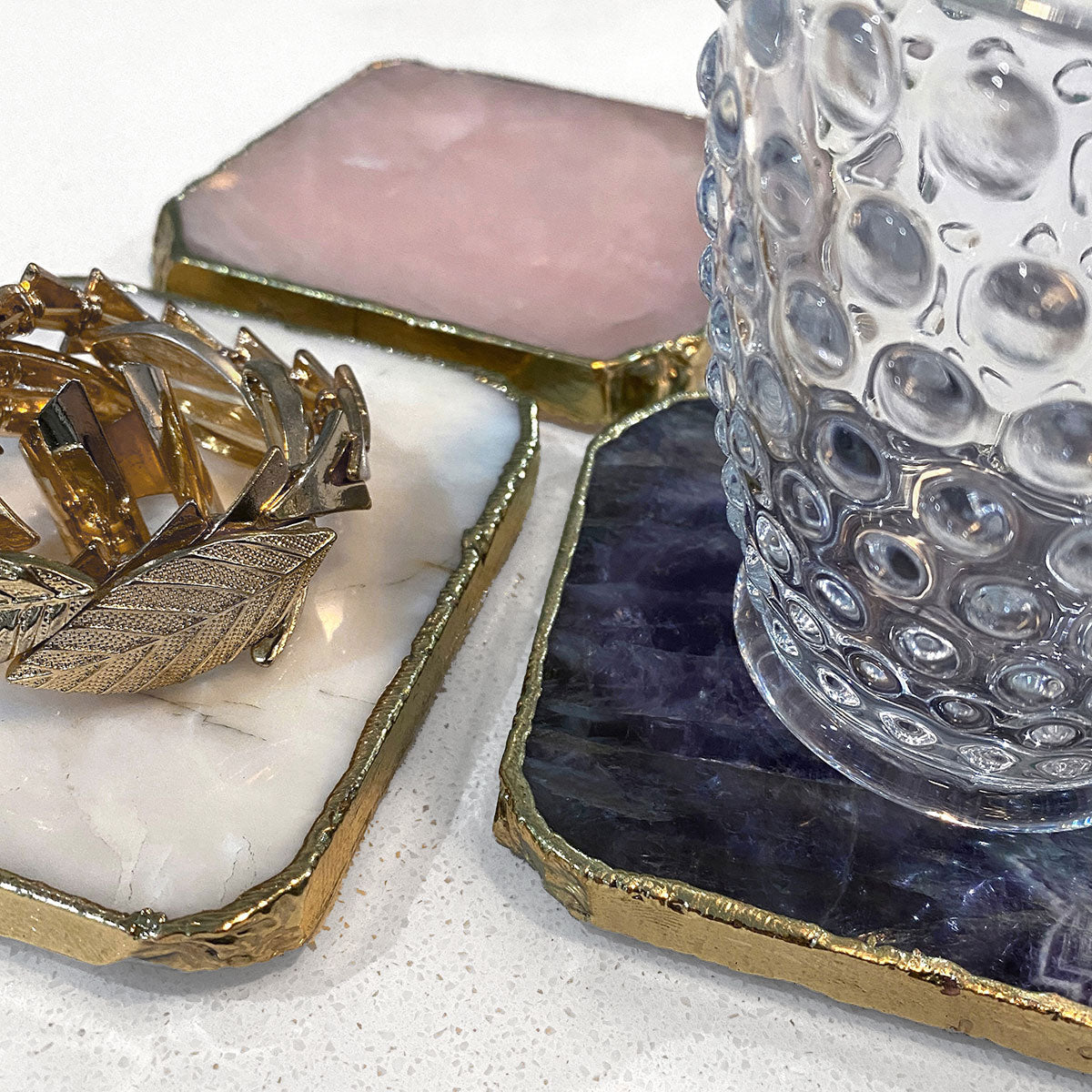 Agate Gold Edged Coasters in White Agate. Shown in situation with a drinking glass and jewellery on top of them, showing all 3 colours.
