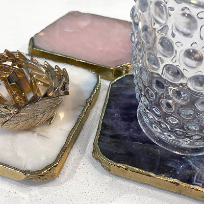 Agate Gold Edged Coasters in Rose Quartz. Shown in situation with a drinking glass and jewellery on top of them, showing all 3 colours.