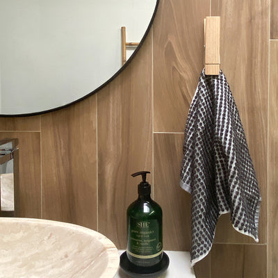 Wood tea towel holder clip shown holding a hand towel in bathroom